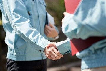 作業着姿の2人が握手を交わす様子