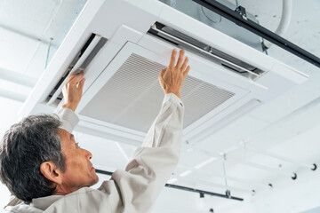 天井埋込型エアコンのパネルを取り付ける作業員